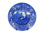 ROYAL DOULTON (A empresa foi fundada em 1815, em Lambeth, Londres, por John Doulton, junto com Martha Jones e John Watts), um (1) prato decorativo confeccionado em faiança inglesa na tonalidade branca, representando Charles Dickens com a Catedral de St. Paul ao fundo na tonalidade azul, apresenta bicado na borda, medindo 25,5cm de diâmetro.