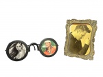 DIVERSOS, dois (2) porta retratos, sendo: A) 1 confeccionado em bronze cinzelado por elementos florais e vegetalistas com bordas em recortes, medindo 20,5x15,5cm e B) 1 duplo no feitio de óculos confeccionado em ferro fundido com pintura preta, sinais de oxidação e mossa na borda, medindo 10,5x27x13,5cm.