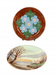 PORCELANA e CERÂMICA, lote com dois (2) pratos decorativos, sendo: A) SCHMIDT, confeccionado em porcelana nacional na tonalidade branca com pintura de paisagem campestre em policromia, medindo 25cm e B) 1 confeccionado em cerâmica vitrificada na tonalidade marrom com pintura floral em policromia, assinado CELIA, medindo 27cm.