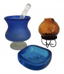 Trio de bibelôs em pasta de vidro colorido sendo um no formato de taca com socador para preparar drinks, um cinzeiro em cristal de Murano azul, e castiçal da Índia na cor âmbar. Pode conter bicado. Medida do maior 15cm.