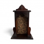 Oratório de parede em madeira, com frontão recortado, interior forrado em tecido brocado e pequeno crucifixo metálico aplicado na parte superior. Interior com tecido adamascado. Peça de devoção doméstica, com pátina original e sinais de uso compatíveis com a idade. Mede 53 cm de altura, 36 cm de largura e 13 cm de profundidade.