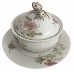 Açucareiro em porcelana francesa, com tampa e pires, decorado com motivos florais delicados em tons rosados e verdes sobre fundo branco. Tampa com pega em forma de frutos, com detalhes em dourado. Conjunto de linhas suaves e elegantes. Discreto bicado. Mede 18 cm diâmetro.