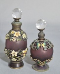 Dois perfumeiros em vidro purpura, guarnições em metal e pedras. Decorados com flores e borboletas esmaltadas. Med. 11 cm do maior.