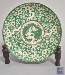 prato decorativo confeccionado em porcelana oriental, de formato circular, com decoração esmaltada em tons de verde, branco, amarelo e detalhes em vermelho, apresentando ao centro dragão estilizado, ladeado por motivos florais e vegetalistas em toda a aba; verso com marca apócrifa em azul sob o vidrado e elementos florais ao redor, medindo 22cm.