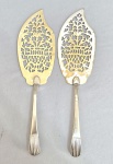 Par de antigas espátulas para bolo ou doce em metal, cinzeladas e fenestradas. Cabos com acabamentos canelados. Com desgastes.Med. 32 cm
