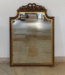 ESPELHO FRANCÊS ESTILO LUÍS XVI - França, ou produção nacional sob influência francesa. Meados  do século XX. Espelho de parede em madeira entalhada e dourada em folha, com frontão decorado por laço central ladeado por rosas e folhagens. Moldura com friso em padrão trançado, cantos superiores recortados em leve curvatura e espelho bisotado. Proporção elegante e muito equilibrada; tamanho ideal para lavabo, aparador, quarto, hall de entrada. Peça decorativa com forte presença estética. Altura - 104 cm. Largura - 73 cm. Condição: Desgastes naturais na douração. Pequenos sinais do tempo na madeira posterior; Espelho íntegro. Estrutura firme. Necessita substituir arame para fixação na parede. Agendamento necessário para retirada pelo n. (21) 96886-7062.