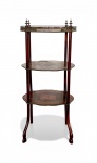 MESA ÉTAGÈRE EM MADEIRA COM MARQUETARIA E GALERIA METÁLICA. Europa ou produção nacional sob influência europeia. Possivelmente do início do século XX. Elegante mesa 'étagère' de três planos, executada em madeira nobre com prateleiras recortadas e decoradas por marchetaria em motivos florais e ornamentos vegetalistas. Os três tampos apresentam composição geométrica e floral em diferentes essências de madeira, formando desenhos centrais e frisos decorativos. O plano superior é circundado por galeria metálica vazada com pequenos pináculos ornamentais, conferindo caráter decorativo e funcional à peça. Estrutura sustentada por quatro colunas torneadas e pernas curvas de perfil gracioso. Peça de pequenas proporções pensada originalmente para apoio de objetos decorativos, porcelanas, pequenas esculturas ou peças de colecionismo. Altura: 70 cm. Largura: 32 cm. Profundidade: 24 cm. Estrutura firme. Atenção: apresenta perda pontual de placagem na prateleira intermediária, conforme pode ser visto na fotografia complementar. Sinais de uso e pátina compatíveis com a idade. Agendamento necessário para retirada pelo n. (21) 96886-7062.