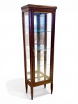 MOBILIÁRIO NACIONAL - Vitrine vertical com tampo em mármore e delicado trabalho de marqueteria. Vitrine vertical em madeira, de linhas esguias, com laterais e porta frontal envidraçadas, permitindo ampla visualização das peças expostas. O interior apresenta três prateleiras em vidro de 2 mm, apoiadas em suportes laterais.O móvel, de produção situada por volta dos anos de 1980, repousa sobre quatro pés afilados, característica associada ao repertório neoclássico tardio. A composição superior é finalizada por tampo em mármore claro. A porta frontal funcional apresenta fechadura com chave, detalhe que reforça a função original de exposição e proteção de objetos delicados, como porcelanas, miniaturas, pequenos bronzes ou joias. A lateral posterior é fechada em madeira, conferindo maior estabilidade estrutural ao móvel servindo de suporte para grande espelho de fundo da vitrine. Altura - 153 cm. Largura - 47,5 cm. Profundidade - 31 cm. Necessita ser lustrada, ou receber verniz de acabamento. Sem indícios de passagem de broca ou pragas. Retirada na Av. Atlântica - bairro do Leme, piso térreo mediante agendamento pelo telefone / whatsApp (21) 96886-7062.