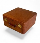 ALTO LUXO VINTAGE- Mala de viagem em formato quadrangular, de perfil alto, marcada por plaqueta metálica fixada frontalmente indicando a casa, G. Magnin & Co. Seattle / Califórnia / USA, anos de 1940. Elegante e grande mala rígida toda confeccionada em finíssimo couro bovino com rara gravação tipo crocodilo, assinada pela tradicional casa americana G. Magnin & Co., Seattle / Califórnia, empresa que atendia a elite da sociedade norte americana da Costa Oeste dos Estados Unidos. A peça ora em Pregão apresenta características únicas de simetria e altura que pode indicar o transporte de acessórios, botas e sapatos. Peça montada em estrutura sólida, com todas as ferragens originais em latão, alça estruturalmente preservada com pequenos desgastes, interior forrado em tecido azul acetinado; presença de cintas de fixação em fitas em excelente estado de conservação. Interior sem manchas, nem rasgos ou partes descosturadas. Peça original que representa o período áureo das viagens transcontinentais, um período no qual aliava-se elegância estética à robustez necessária às viagens de longa duração. *Estado de conservação excepcional para um item da década de 40. Desgaste leve na alça. Descrição técnica do item - Mala de viagem rígida em Couro bovino com gravação tipo crocodilo e costura manual perimetral íntegra. Ferragens em latão dourado com fechos originais funcionando. Forração interna em tecido azul acetinado, com fitas de fixação em excelente estado. Presença da plaqueta metálica original da casa G. Magnin & Co.Medidas Mala quadrada - 51 cm X 51 cm X 24 cm.Nota do editor - A casa, G. Magnin & Co. foi uma das mais sofisticadas casas de luxo dos Estados Unidos, fornecedora de artigos exclusivos para a elite da Costa Oeste, com forte ligação ao universo das grandes viagens transcontinentais e marítimas do século XX.Fundada em 1876, em San Francisco, por Joseph MagninTornou-se uma das mais sofisticadas lojas de luxo dos Estados Unidos, rivalizando com Bergdorf Goodman e Saks.Sua especialidade foi artigos de moda e vestuário de alta costura importada da Europa; artigos de viagem de alto padrão (como mostra esse exemplar) eacessórios sob encomenda. *A G. Magnin não fabricava diretamente os itens que vendia: ela encomendava a produção a oficinas especializadas (EUA e Europa), aplicando sua marca como selo de curadoria e padrão de luxo. Item faz conjunto com os dois lotes anteriores. * ATENÇÃO; LOTE EXCLUSIVAMENTE DE UMA MALA APENAS (A DE BAIXO). A IMAGEM COMPLEMENTAR É MERAMENTE ILUSTRATIVA E SERVE PARA MOSTAR O CONJUNTO COMPLETO. DEMAIS MALAS SÃO OBJETO DE LOTES ANTERIORES.