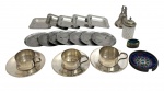 Lote com conjunto de peças diversas em metal prateado, composto por 3 xícaras com pires, 5 pequenas travessas retangulares, 7 bases circulares, saleiro/pimenteiro, pequeno sino decorativo e dois objetos ornamentais, incluindo peça esmaltada. Apresenta sinais de uso e oxidação. Total de 21 peças, medida do maior 10cm.
