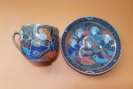SATSUMA - "Imperatriz e seus guardiões" - Grande xícara de café e seu respectivo pires em porcelana japonesa de coleção Satsuma Imperial. Peças ricamente policromadas e com acabamento em fios de ouro. Apresenta fio de cabelo na xícara - Dimensões: 7,5 x 9 cm (xícara) 15 cm (pires)