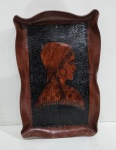 Antigo Quadro decorativo em couro retratando uma mulher com vestimentas tradicionais, incluindo um lenço na cabeça e um xale com franjas .Medindo 51 x 33 cm