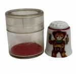 Reutter Porzellan  Dedal de porcelana alemã, decorado com figura infantil (ursinho), marca impressa na base. Acompanha estojo cilíndrico original em acrílico com base em veludo. Peça colecionável, acabamento esmaltado, em bom estado geral, com leves sinais do tempo no estojo.