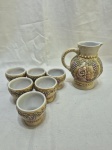 Jarra com 6 copinhos em porcelana Ceramarte ricamente trabalhada com relevos. Medindo a jarra 16cm de altura, copos 7cm x 6,5cm de altura.