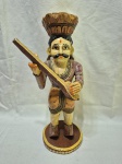Escultura decorativa artesanal em madeira entalhada e policromada, representando figura masculina de músico Rajasthani em trajes tradicionais, com bigode característico, mãos em gesto de saudação/oferta, apoiada sobre base circular em madeira, apresentando pátina do tempo e desgastes naturais da policromia, peça de caráter étnico e decorativo. Medindo 33cm de altura. Com perda no esmalte.