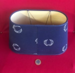 Cúpula de abajur em formato oval, apresentando uma cor azul-marinho com um padrão repetitivo de coroas de louros em dourado no estilo império  dos meados do século XX.
