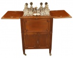 Este bar de coquetéis inglês é particularmente incomum e elegante. Feito de nogueira cor de mel, cerca 1910/1920, possui quatro pés retos com rodinhas e compartimentos em cada lateral para guardar garrafas e biscoitos. Sua tampa é articulada, com uma abertura bipartida que revela uma plataforma elevatória, equipada com um conjunto completo de requintados 06 garrafas de cristal, uma petisqueira em metal inglês prateado, 02 galheteiros, 12 copos tamanhos diversos. Dentro da parte superior. Quando fechado, ele se dobra suave e automaticamente graças ao seu elaborado mecanismo interno. É um verdadeiro bar surpresa; do lado de fora, não se imagina o que há dentro, mas quando aberto, é de tirar o fôlego com sua plataforma elevatória repleta de garrafas copos de cristal. Este bar metamórfico adicionará um toque de classe a qualquer estilo de decoração e certamente será um ótimo assunto para iniciar conversas. Quando aberto, mede 124 cm de comprimento x A. 90 x P. 51 cm. Fechado: A. 90 x C. 64 x P. 51 cm.