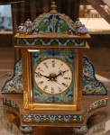 Relógio de mesa, mostrador com algarismos romanos, gabinete em cloisonné policromado com predominância da tonalidade azul sobre latão, frontal com cristal bisotado, ilhargas com esmaltações representando bustos femininos, movimento quartz, não testado.               Medidas: Alt. 21 x 21 x 09 cm.