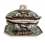 Sopeira em cerâmica, manufatura portuguesa, acompanhada de presentoir e colher. Decoração em esmalte policromado, representando ramos, flores e elementos zoomórficos.  Medidas: sopeira (10 x 8 x 8 cm); presentoir (12,5 x 10 cm); colher (9,5 cm de comprimento). Apresenta sinais de uso e pátina compatíveis com a idade