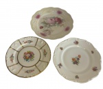 Três pratos em porcelana europeia de diferentes manufaturas, com decoração em esmalte policromado, apresentando motivos florais e detalhes em relevo e douração nas bordas. Medidas: 21 cm; 20 cm; e 18,5 cm de diâmetro.