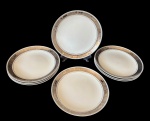 Steatita - Oito pratos rasos em porcelana com aba decorada em tom prateado e detalhes em relevo formando cenas clássicas ao redor da borda. Filete fino próximo à área central. Medindo: 24,5 cm.