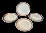Steatita - Oito pratos rasos em porcelana com aba decorada em tom prateado e detalhes em relevo formando cenas clássicas ao redor da borda. Filete fino próximo à área central. Medindo: 24,5 cm.