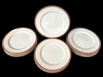 Doze pratos rasos em porcelana japosena na cor branca, decorada em tom dourado com padronagem geométrica contínua, além de filete fino próximo à área central. Manufatura no verso. Medindo: 26 cm.