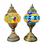 Dois abajures com estrutura em metal trabalhado, apresentando base e acabamento em tom dourado envelhecido, com detalhes em relevo e recortes decorativos na parte superior. Cúpulas em vidro com aplicação de mosaico artesanal, compostas por pequenos fragmentos coloridos formando padrões geométricos, funcionando. Medindo: 29 x 13 cm. Um apresenta desgaste/ oxidação na base.