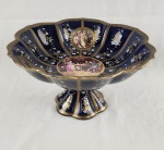 Centro de mesa em porcelana azul cobalto , possivelmente francesa de LIMOGES, comintricados desenhos e pintura floral com bordas em ouro. Possui cenas galantespintadas ao centro e em medalhões ao redor. É moldado com bordas onduladas emestilo clássico e luxuoso sobre base longa escalonada. Medindo: 20 x 35 cm.