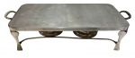 Rechaud retangular em metal prateado com suporte elevado, duas bases para aquecimento, alças laterais e tampa superior. Medindo: 13 x 48,5 x 23,5 cm.