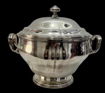 Sopeira em metal prateado com tampa, alças laterais e base elevada, apresentando acabamento polido. Medindo:  30,5 x 24 x 25 cm.