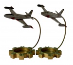 Par de cinzeiros decorativos em metal com design de avião em voo, sustentado por haste curva sobre base em formato de engrenagem, estilo vintage/industrial, cada peça mede aproximadamente 20 cm de altura, 16 cm de largura e 19,5 cm de comprimento.