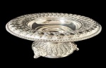 Elegante fruteira / centro de mesa executado em metal espessurado à prata, com rico trabalho em relevo e detalhes ornamentais que remetem ao estilo clássico; mede aproximadamente 36 cm de diâmetro por 13,5 cm de altura,