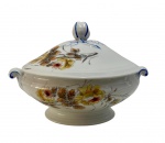 Sopeira em porcelana com tampa, decorada com motivos florais policromados em tons de amarelo, ocre e vermelho, acompanhados por traços sutis em azul. Tampa com pega superior em formato orgânico. Medidas: 26 x 22,5 cm.