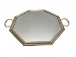 Bandeja espelhada de formato octogonal, com estrutura em metal de tonalidade dourada, apresentando borda ricamente trabalhada com frisos e motivos ornamentais em relevo. Possui duas alças laterais com acabamento torcido. Fundo em espelho. Medida: 48,5 cm.