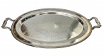 Bandeja em metal espessurado a prata, de formato oval, apresentando alças laterais trabalhadas e borda com delicado acabamento perolado, parte central ricamente ornamentado com gravações em arabescos e motivos florais. Superfície levemente côncava. Medidas: 50 x 30 cm