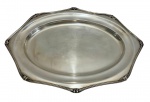 Travessa em metal espessurado a prata, de formato oval, borda recortada com elegante trabalho em relevo. Possui superfície lisa com leve cavidade central. Medidas: 46 x 23 cm. Apresentando sinais naturais do tempo, como pequenos riscos superficiais e leves desgastes no banho.