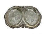 Petisqueira em metal espessurado a prata, ricamente trabalhada em cinzel com decoração em relevo de flores, conchas e volutas, refinamento ornamental de inspiração clássica, acompanhada de recipientes em vidro moldado perfeitamente encaixados à estrutura, unindo praticidade e elegância ao conjunto; medidas: travessa 3,5 x 43,5 x 31 cm e recipientes 3 x 24 x 15,5 cm.