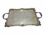 Antiga bandeja em metal espessurado a prata, de formato retangular com cantos recortados, ricamente ornamentada com bordas trabalhadas em volutas e frisos em relevo, apresentando delicada decoração gravada ao centro com motivos florais e arabescos, possuindo alças laterais integradas, medidas: 53 x 32,5 cm