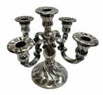 Antigo candelabro em metal espessurado a prata, de cinco braços, apresentando corpo central torneado com rica decoração em relevo e braços curvilíneos com volutas, sustentando suportes com bordas onduladas, apoiado sobre base trabalhada; medidas: 21,5 x 20,5 x 20 cm;