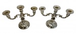 Par de candelabros em metal espessurado a prata, de três braços cada, apresentando corpo central torneado com elegante decoração em relevo e braços curvilíneos com volutas, sustentando suportes com bordas onduladas, apoiados sobre base trabalhada; medidas: 22,5 x 28 x 12 cm;