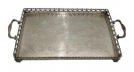 Bandeja com alças em metal espessurado a prata, de formato retangular, apresentando borda vazada trabalhada em arabescos e interior com delicada decoração gravada, apoiada sobre pequenos pés; medidas: 7,5 x 47,5 x 25,5 cm.