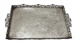 Antiga bandeja em metal espessurado a prata, com borda vazada ricamente trabalhada e alças laterais ornamentadas. Fundo com textura martelada. Medidas: 41 x 24,5 x 3 cm.