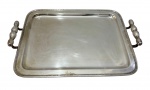 Bandeja em metal espessurado a prata, de formato retangular, com alças laterais e borda decorada em friso geométrico. Apresenta sinais de uso compatíveis com o tempo, sendo que uma das alças necessita de restauro. Medidas: 47,5 x 32,5 x 5 cm.