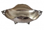 Floreira em metal espessurado a prata, de formato oval com bordas onduladas, apresentando alças laterais ricamente trabalhadas e pés decorados. Medidas: 8 x 23 x 11 cm.