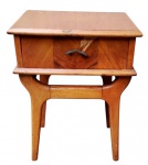 Mesa de cabeceira em madeira, de meados do século XX , com uma gaveta frontal e base de linhas orgânicas características do período. Apresenta sinais de uso e necessita restauro. Medidas: 52 x 41 x 31 cm.