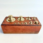 Antigo conjunto de pesos para balança confeccionados em bronze, acondicionados em cepo de madeira composto por 10 pesos. Med 20 x 8,5 cm.