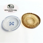 Lote com dois cinzeiros, sendo um em grosso vidro na cor âmbar e outro em porcelana alemã manufatura Hutschenreuther. Med 16 x 5 cm e 15 x 3 cm.