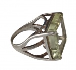 Anel em prata com design vazado e contemporâneo, apresentando estrutura robusta e bem trabalhada, adornada por pedra de formato retangular em tonalidade verde suave, lapidada em facetas. Assinado Sauro. Aro: 24. Peso: 12 g