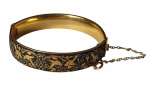 Bracelete antigo em metal dourado, com acabamento banhado, apresentando decoração em esmaltação preta com delicados motivos ornamentais e pássaros em tonalidade dourada. A peça possui fecho articulado com corrente de segurança. Medida: 7 cm de diâmetro